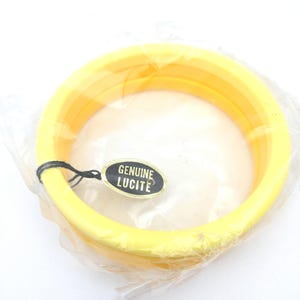 Puede incluir: Un conjunto de tres brazaletes amarillos de Lucite, aún en su embalaje original. Las pulseras son de color amarillo brillante y sólido. La etiqueta dice "GENUINE LUCITE".