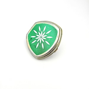 May include: A small, vintage compact with a silver-toned metal frame. The compact features a bright green enamel top with a white floral design. The compact is a unique accessory.
