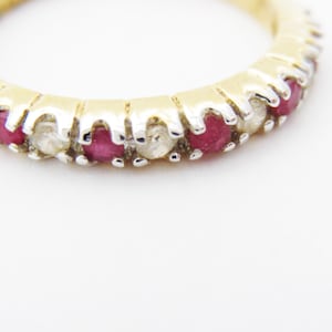 Może przedstawiać: Złoty pierścionek z rzędem naprzemiennych czerwonych rubinów i białych diamentów.