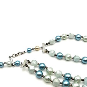 May include: A two-strand necklace featuring faux pearls in shades of blue, white, and light green. The necklace has a silver-tone clasp and chain. The pearls are round and evenly spaced, creating a classic and elegant look.