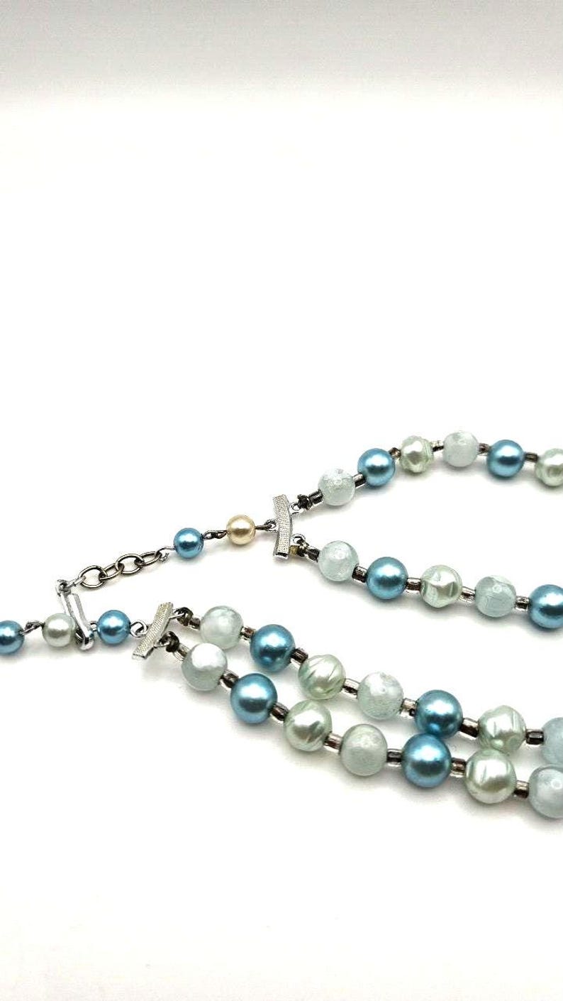 May include: A two-strand necklace featuring faux pearls in shades of blue, white, and light green. The necklace has a silver-tone clasp and chain. The pearls are round and evenly spaced, creating a classic and elegant look.