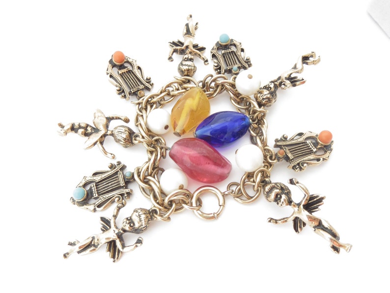 May include: A gold charm bracelet with multiple charms, including cherubs, lyres, and colorful glass beads. The bracelet has a lobster clasp closure.