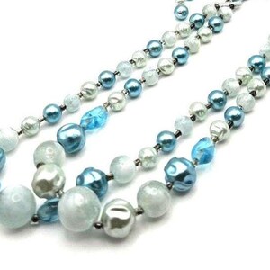 May include: A multi-strand necklace featuring a mix of blue, teal, and white beads. The beads vary in size and shape, including round and irregular forms. The necklace is displayed against a white background, highlighting the colors and textures of the jewelry.