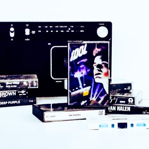 May include: A collection of vintage VHS tapes featuring bands like Tool, Deep Purple, Savoy Brown, and Van Halen. The tapes are stacked on top of each other and are in various states of wear and tear.