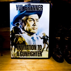 May include: A movie poster for "Invitation to a Gunfighter" featuring Yul Brynner. The poster has a vintage aesthetic with a portrait of Brynner and action scenes. The title is prominently displayed in bold text.