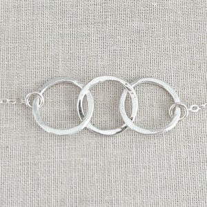 May include: A silver necklace with three interlocking circles. The circles are hammered and have a textured finish.