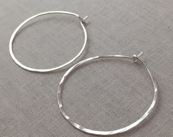 May include: A pair of silver hoop earrings with a hammered finish. The earrings are simple and elegant, and would make a great gift for any occasion.