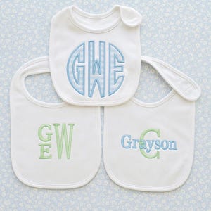 May include: Three white baby bibs with embroidered initials and names. One bib features the initials "GHE" in a blue and white striped pattern. Another has "GW" in green, and the third says "Grayson" in blue and green.