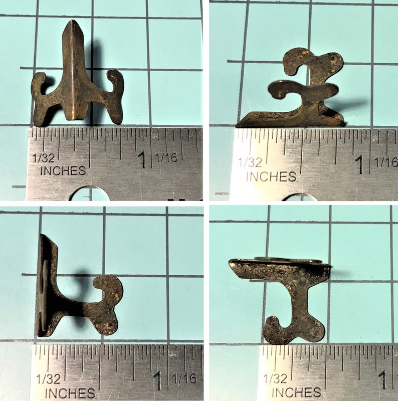 Op de afbeelding: Vier antieke metalen fotostandaards. Elke standaard is ongeveer 2,5 cm hoog en heeft een uniek ontwerp. De standaards zijn gemaakt van donker metaal met een rustieke afwerking.