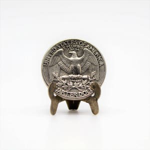 Op de afbeelding: Een zilveren Amerikaanse kwart dollar munt met de afbeelding van een adelaar op de voorkant en de woorden "United States of America" en "Quarter Dollar" rond de rand.