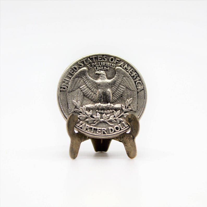 Op de afbeelding: Een zilveren Amerikaanse kwart dollar munt met de afbeelding van een adelaar op de voorkant en de woorden "United States of America" en "Quarter Dollar" rond de rand.