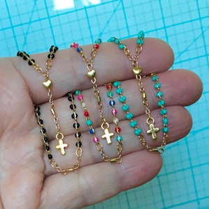 May include: Five beaded necklaces with gold cross and heart charms. The necklaces are black, turquoise, red, white, and pink.