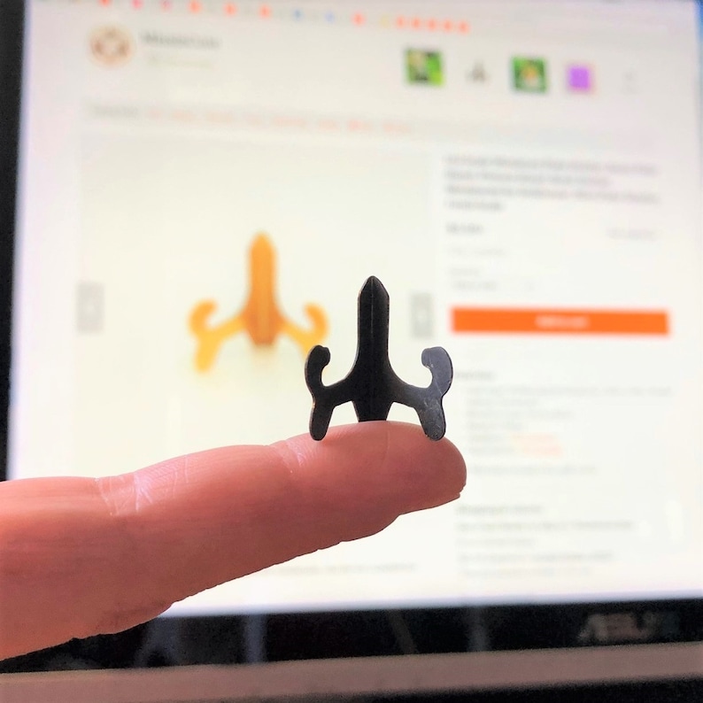 Op de afbeelding: Een kleine zwarte metalen displaystandaard voor het presenteren van kleine items zoals beeldjes of sieraden. De standaard heeft een driehoekige basis met drie gebogen armen.