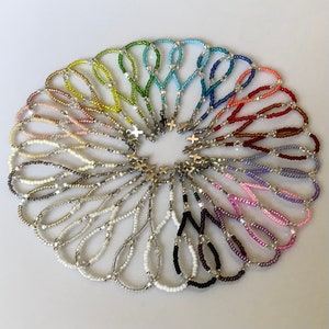 May include: A set of 20 colorful beaded bracelets with silver cross charms. Each bracelet is made with small beads in a variety of colors, including pink, purple, blue, green, yellow, and red.