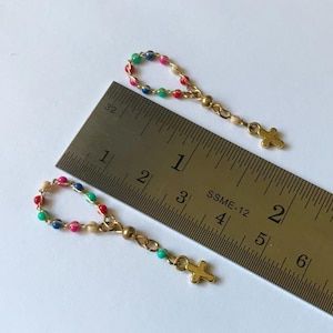 May include: Two miniature rosaries with colorful beads and gold-colored crosses. The beads are in shades of red, green, blue, pink, and cream. A metal ruler is in the image, showing the rosaries are approximately 1.5 inches in length.