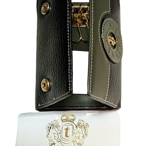 May include: A black and green leather key holder with a gold metal key ring and a gold metal logo that says "a. testoni" and "Bologna-Italia".