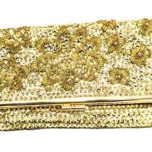 May include: A gold clutch purse with a floral design made of sequins. The purse has a metal clasp.