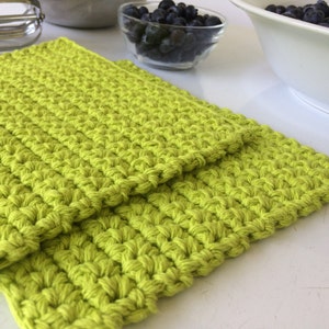 May include: Two lime green crocheted dishcloths stacked on top of each other. The dishcloths are made with a textured stitch.