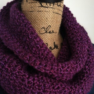 May include: A purple crocheted infinity scarf. The scarf is made with a chunky yarn and has a textured look.