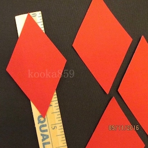 May include: Five red diamond-shaped paper cutouts on a black background. A wooden ruler with the word "QUAL" printed on it is visible in the bottom left corner of the image. The date "05/11/2016" is printed in the bottom right corner of the image.