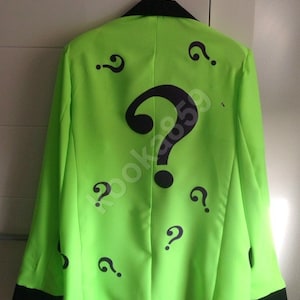 May include: A green blazer with a black collar and black trim on the sleeves. The blazer is covered in black question marks.