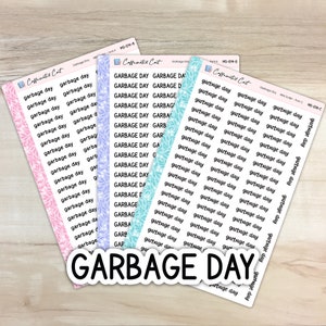 May include: Three sheets of stickers with the text "Garbage Day" repeated multiple times in different fonts and sizes. The stickers are on a light wood background. The stickers are in pink, blue, and green.