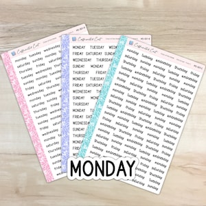 May include: Three sheets of stickers with days of the week written in black script. The sheets are pink, blue, and turquoise with a leaf pattern. The words "MONDAY" are written in large black letters on a white background.