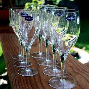 May include: A set of clear glass wine glasses with slender stems and circular bases. Each glass features a small, dark blue oval sticker near the rim with the white text Luigi Bormioli Italy printed on the surface of the glass bowl.