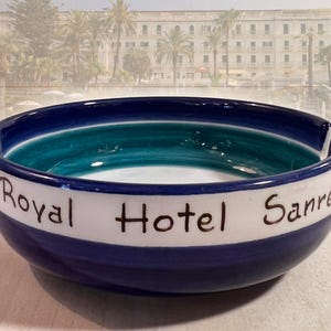 May include: A blue and white ceramic ashtray with the words "Royal Hotel Sanremo" written on it. The ashtray has a teal green stripe around the inside.