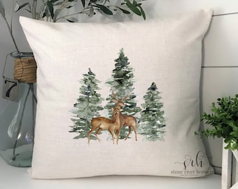May include: A white throw pillow featuring a watercolour design of two deer standing in a forest of green trees. The pillow has the text "srh stone river home co" in the bottom right corner.