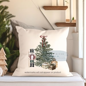 May include: A white pillow with a watercolor illustration of a Christmas tree, a nutcracker, and presents. The text "River & Co. A Home Studio" is in a circle on the pillow. The text "watermarks will not appear on product" is at the bottom of the pillow.