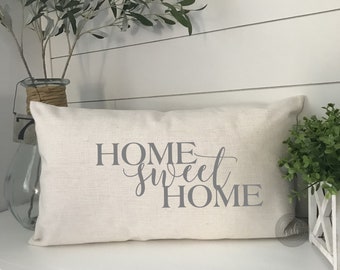 May include: A white throw pillow with the text "HOME sweet HOME" in gray lettering. The pillow is on a white shelf with a green plant in a white planter.