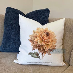 May include: A white pillow with a large, orange-brown dahlia flower printed on it. The flower is in focus and the background is blurred. The pillow is on a couch with a blue pillow behind it. The text "watermarks will not appear on final product" is at the bottom of the pillow.