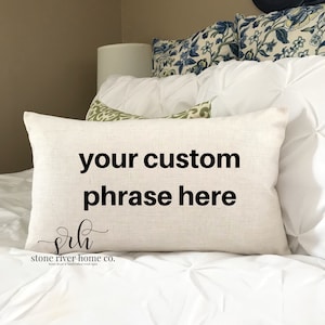 May include: A white throw pillow with the text "your custom phrase here" and the logo "srh stone river home co." in black lettering.