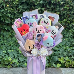 May include: A bouquet of plush toys featuring characters from the popular K-pop group BTS and the BT21 line of characters. The bouquet is wrapped in purple paper and includes artificial flowers.