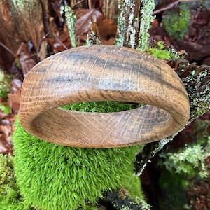 May include: A handcrafted wooden bracelet with a natural wood grain pattern. The bracelet is a warm brown color and has a smooth, rounded shape. The bracelet is approximately 3 inches in diameter.