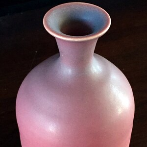 Op de afbeelding: Een roze keramische vaas met een brede basis en een smalle hals. De vaas heeft een kleurverloop, beginnend met een donkerder roze aan de onderkant en vervagend naar een lichter roze aan de bovenkant.