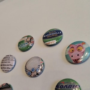 May include: A collection of seven round, colorful buttons with various Disney park attractions and characters. The buttons feature images of Frozen, Remy's Ratatouille Adventure, Guardians of the Galaxy, Soarin', and a pink character from a Disney movie.