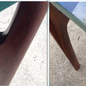 K&ouml;nnte beinhalten: Nahaufnahme eines Tisches aus dunklem Holz mit einer Glasplatte. Der Tisch hat ein einzigartiges Design mit abgewinkelten Beinen.