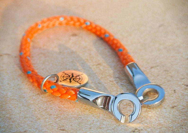 May include: Orange rope bracelet with a compass charm and silver metal clasp.