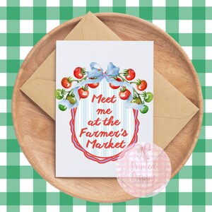 Op de afbeelding: Een wenskaart met de tekst "Meet me at the Farmer's Market" omringd door een aquarel illustratie van tomaten en een blauwe strik. De kaart ligt op een houten dienblad met een bruine envelop, tegen een groen-witte geruite achtergrond.
