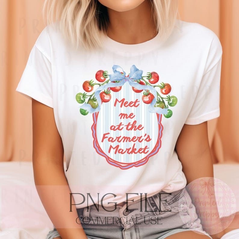 Op de afbeelding: Wit T-shirt met een aquarelontwerp met de tekst "Meet me at the Farmer's Market". Het ontwerp toont rode en groene tomaten en een blauw lint. Het shirt is een PNG-bestand voor commercieel gebruik.