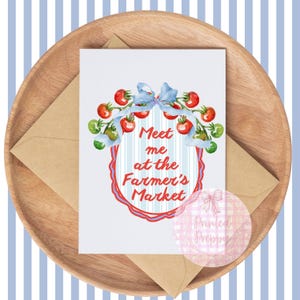 Op de afbeelding: Een wenskaart met de tekst "Meet me at the Farmer's Market" omringd door een aquarel illustratie van tomaten en een blauwe strik. De kaart ligt op een houten dienblad met een kraft papieren envelop.