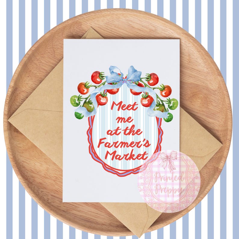 Op de afbeelding: Een wenskaart met de tekst "Meet me at the Farmer's Market" omringd door een aquarel illustratie van tomaten en een blauwe strik. De kaart ligt op een houten dienblad met een kraft papieren envelop.