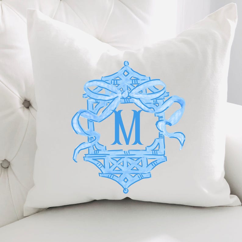 May include: White square throw pillow with a light blue monogram design. The design features a decorative frame with a bow and the letter "M" in the center. The pillow is on a white surface.