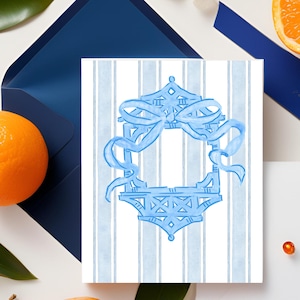 May include: A greeting card with a blue and white striped background. The card features a light blue decorative frame with a bow design. An orange and a blue envelope are in the background.