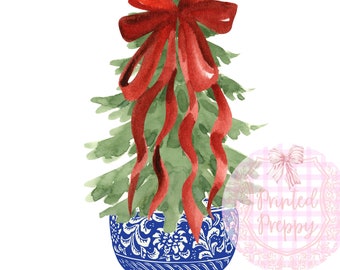Puede incluir: Un pequeño árbol de Navidad verde con un gran lazo rojo se sienta en una maceta de porcelana azul y blanca. La maceta tiene un diseño floral.