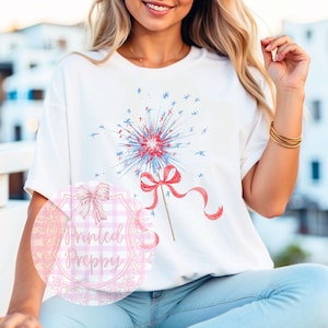 K&ouml;nnte beinhalten: Ein wei&szlig;es T-Shirt mit einem rot-wei&szlig;-blauen Feuerwerksdesign. Das Feuerwerk ist mit einer roten Schleife verziert. Das Shirt tr&auml;gt die Worte "Printed Preppy" in Pink auf einem rosa-wei&szlig; karierten Hintergrund.