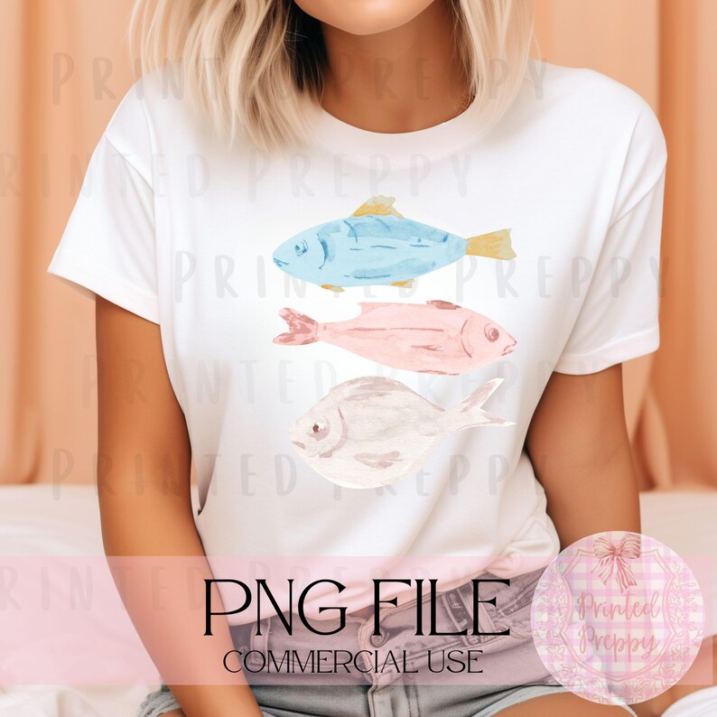 Puede incluir: Una camiseta blanca con un dise&ntilde;o de tres peces de acuarela. Los peces son azules, rosas y blancos. El texto "PNG FILE COMMERCIAL USE" est&aacute; en la parte inferior de la camiseta.