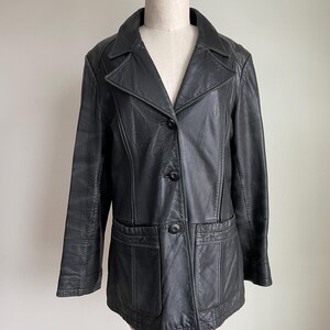 May include: A black leather jacket with a classic design. The jacket features a notched collar, two front pockets, and a three-button closure. The jacket is displayed on a mannequin against a neutral background.